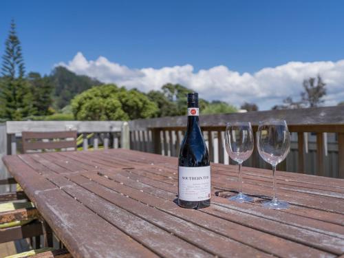 a bottle of wine sitting on a wooden table with two wine glasses at Family Oasis - Pauanui Holiday Home in Pauanui