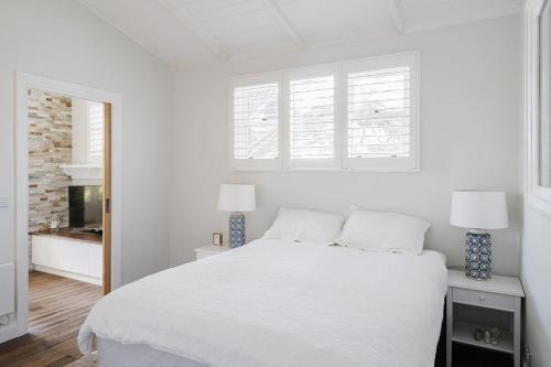 a white bedroom with a white bed and two lamps at Cottage Enchantment Blooming Garden Getaway in Red Hill South