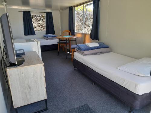 Zimmer mit 2 Betten, einem TV und einem Tisch in der Unterkunft Picton's Waikawa Bay Holiday Park in Picton