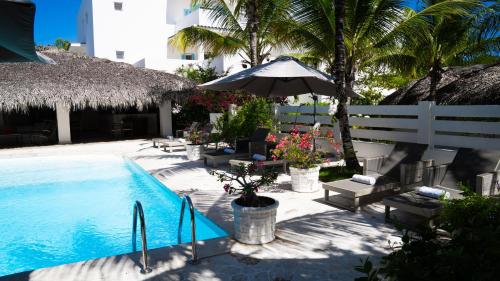 una piscina con sillas y una sombrilla junto a un edificio en Boutique Hotel Las Flores Punta Cana, en Punta Cana