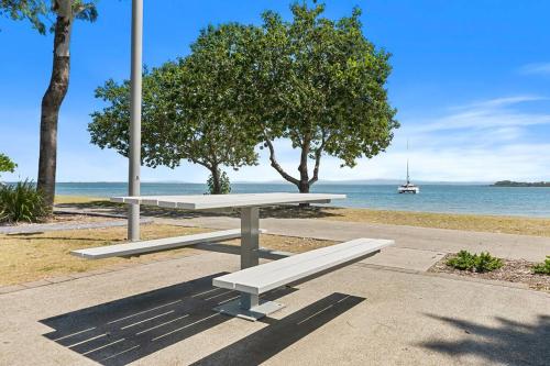 a white bench sitting on a sidewalk near the water at Bongaree Water's View in Bongaree