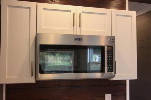 a microwave in a kitchen with white cabinets at Tiny House Oasis: Nature Escape in Nacogdoches