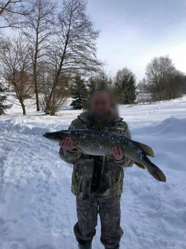 a man in camouflage holding a fish in the snow at Будинки рибалки in Sudovaya Vishnya