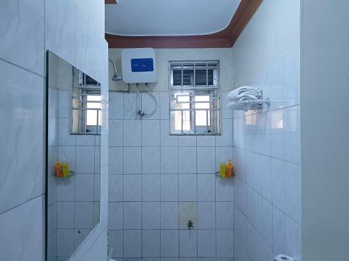 a white tiled bathroom with a shower and a window at Amaryllis blue,8mins source to River Nile,secure, peaceful, central great location in Jinja