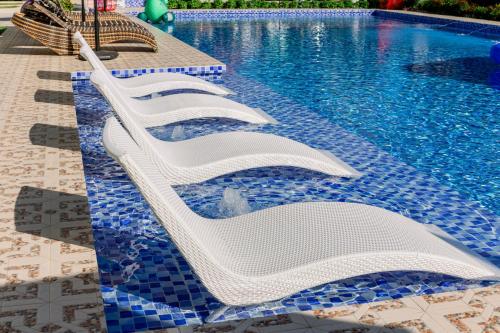 a row of white lounge chairs next to a swimming pool at Sonrisa Resort De Playa by Hiverooms in San Remigio