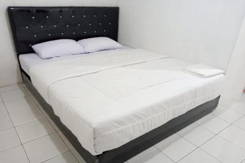 Bett mit schwarzem Kopfteil und weißer Bettwäsche in der Unterkunft Capital O 93728 Guest House Cemara in Bandung