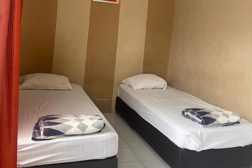 2 bedden in een kamer met witte lakens en kussens bij OYO 93749 Aksana Homestay Syariah in Pekanbaru