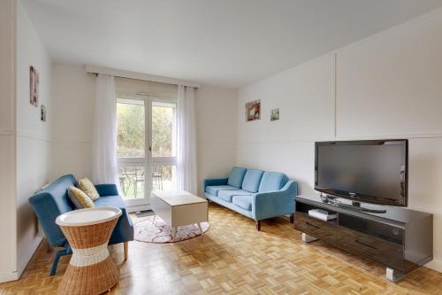 sala de estar con 2 sillas azules y TV de pantalla plana en La "Marquise", Jardin et Parking Privatif en Guyancourt