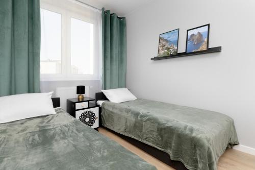 een slaapkamer met 2 bedden, groene gordijnen en een raam bij Apartment in Gdańsk with 3 Bedrooms, Furnished Balcony and 2 Desks by Rent like home in Gdańsk