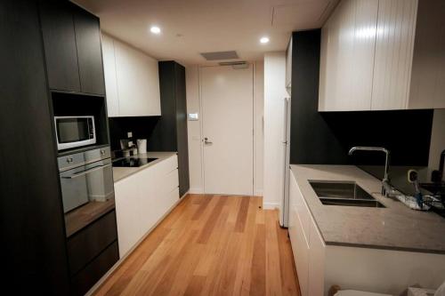 cocina con armarios blancos y suelo de madera en Braddon 1BR Apt, WiFi, Secure Parking, AMAZING LOCATION en Canberra
