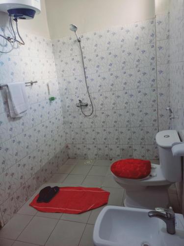 La salle de bains est pourvue d'une douche et de toilettes avec un siège rouge. dans l'établissement Peace N Quiet aux Almadies, à Dakar