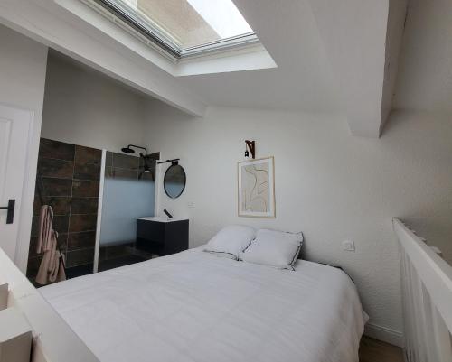 une chambre avec un lit blanc et une lucarne dans l'établissement AGENCE DU SACRE COEUR Immobilier, à Perpignan