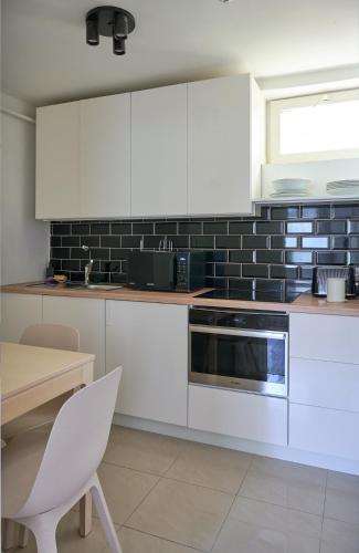 a kitchen with white cabinets and a black tile wall at Bükfalva Kúria apartmanház in Bük