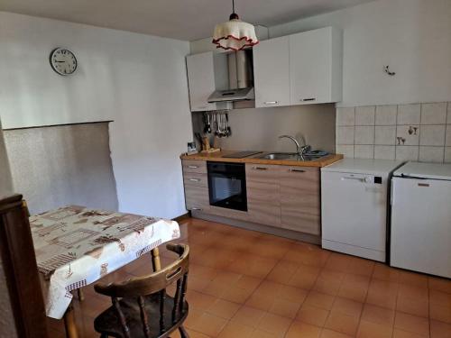 uma cozinha com armários brancos, uma mesa e um lavatório em casetta in montagna em Mocenigo