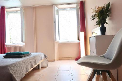 um quarto com uma cama, uma cadeira e janelas em City Garni em Martigny-Ville
