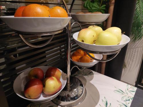 three bowls of fruit on a stand with apples and oranges at Hôtel Rallye & Entrées aux Bains de la Gruyère in Bulle