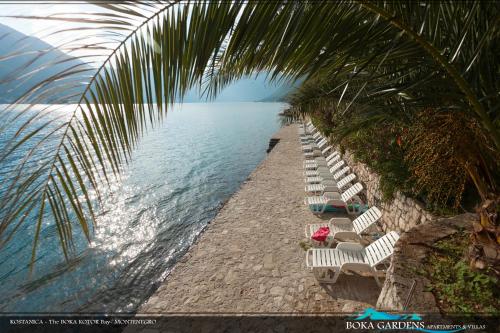 eine Reihe von Gartenstühlen neben dem Wasser in der Unterkunft Boka Gardens Seaside Resort in Kotor