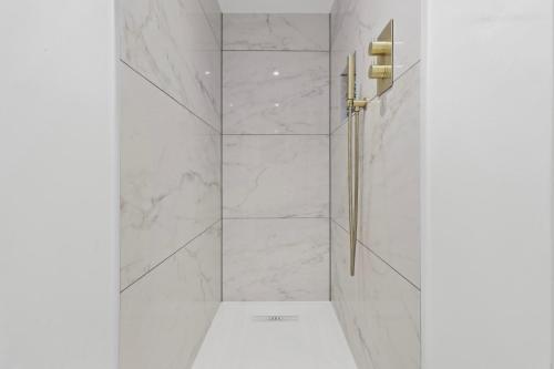 Baño blanco con ducha y paredes de mármol en Chic Urban Retreat: Modern Apartment in Eastbourne, en Eastbourne