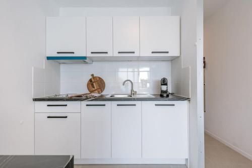una cocina con armarios blancos y fregadero en Modern studio near the beach, en Ostende