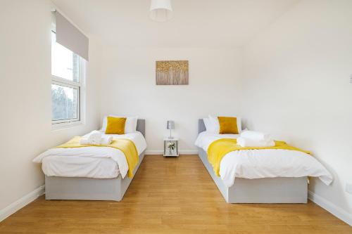 雷恩漢姆的住宿－Heads-On-Beds Rainham Essex - 4Bedrooms with Garden，配有白色墙壁和木地板的客房内的两张床