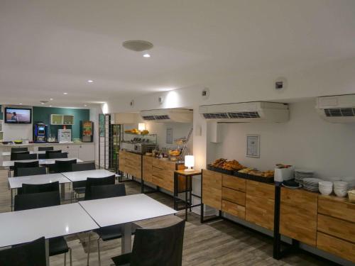una sala da pranzo con tavoli e sedie e una cucina di ibis Styles Saint Julien en Genevois Vitam a Neydens