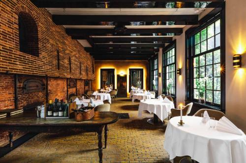 un restaurante con mesas y sillas blancas y ventanas en The Dylan Amsterdam - The Leading Hotels of the World en Ámsterdam