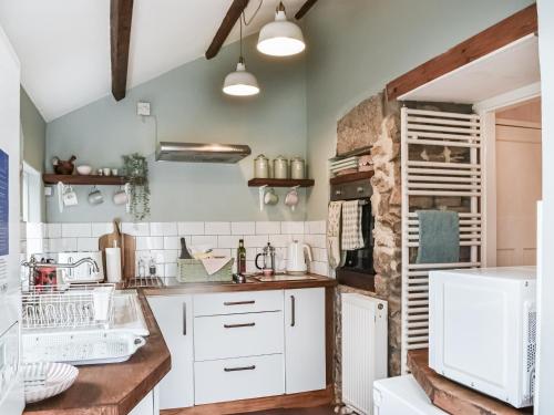 a kitchen with white cabinets and a stone wall at Middles Cottage in West Woodburn
