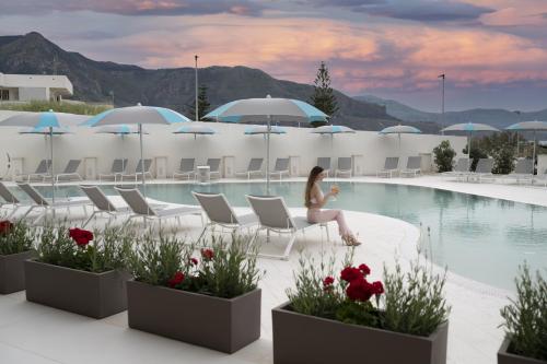 a woman sitting on a chair next to a swimming pool at Resort La Battigia Beach & Spa in Alcamo Marina