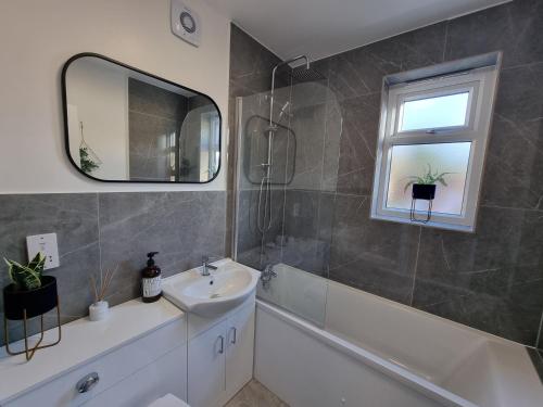 a bathroom with a sink and a tub and a mirror at Cute Cottage in Egham Heathrow- 7 Guests 3 bedrooms in Egham