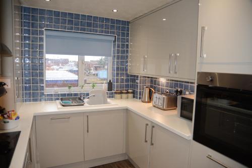 a kitchen with white cabinets and a blue tiled wall at Peaceful Waterfront Apartment, Private Parking, Hull Marina in Hull
