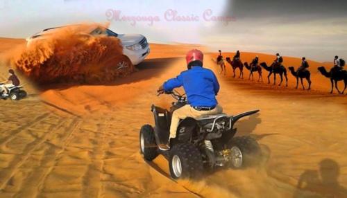 a man on a four wheeler in the desert with a group of camels at Merzouga Authentic Camps in Merzouga