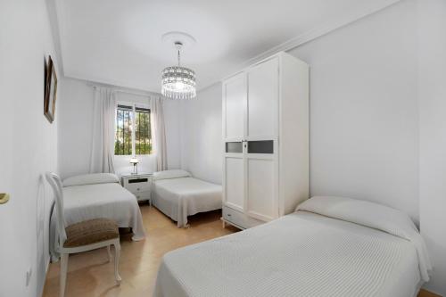 a white bedroom with two beds and a chandelier at Apartamento Altamar in Novo Sancti Petri
