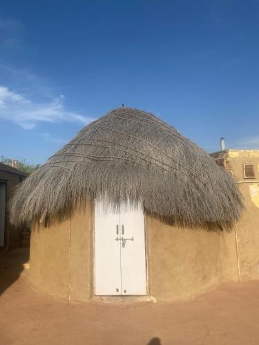 a small hut with a grass roof with a white door at Jaisalmer Safari Base & Camp in Khuri