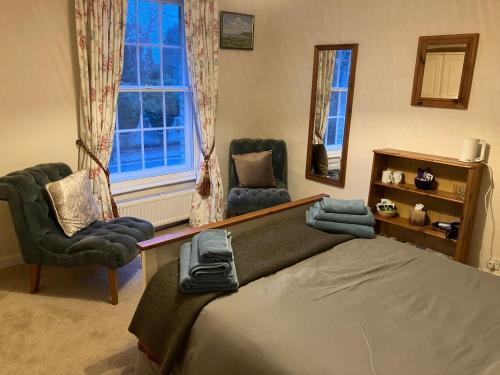 a bedroom with a bed and two chairs and a window at Yew Tree House, Bed & Breakfast in Colchester in Lexden