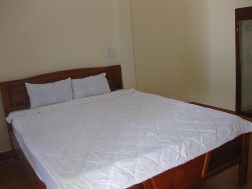 a bed with a wooden frame and white sheets at Cocosand Hotel in Mui Ne