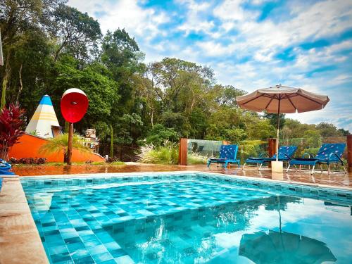 ein Pool mit einem Sonnenschirm, einigen Stühlen und einem Sonnenschirm in der Unterkunft Casa de Vidro - Vila Mágica in Bueno Brandão