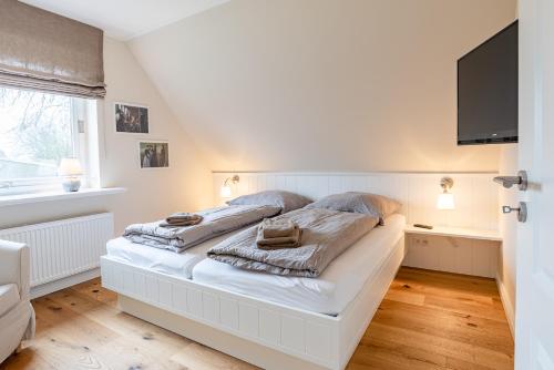 a bedroom with a white bed with a flat screen tv at White House Ferienwohnung 2 in Alkersum
