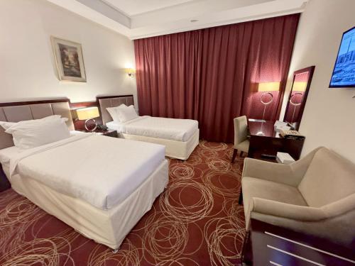 a hotel room with two beds and a chair at فندق أبراج الريان المكية Al Rayyan Makiya Towers Hotel 1 in Makkah
