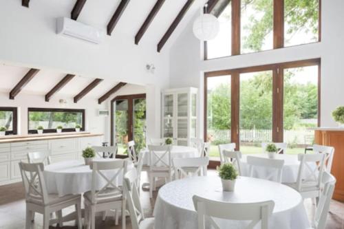 une salle à manger avec des tables blanches, des chaises et des fenêtres dans l'établissement Cottage im Natur-Resort Pool, Schwimmteich & Sauna, à Kiskunmajsa