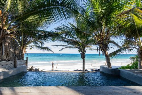 a swimming pool next to a beach with palm trees at UMi Tulum in Tulum