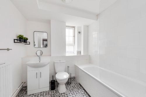 a white bathroom with a toilet and a tub and a sink at Sleek Shoreditch Hideout - 2 Bed Gem with Balcony in Central London in London