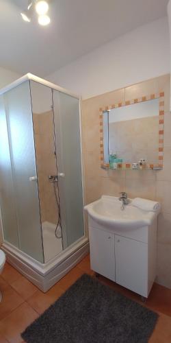 ein Bad mit einer Dusche, einem Waschbecken und einem Spiegel in der Unterkunft Apartmani Bašić 2 in Njivice