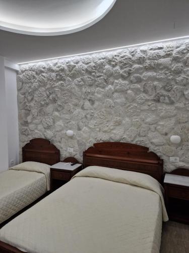 a bedroom with two beds and a stone wall at Emmanouela Studios & Villas in Karterados