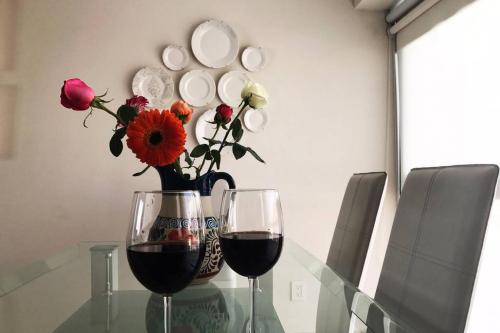 two glasses of wine and a vase with flowers on a glass table at Cerca de hospital infantil wtc centrico y seguro! in Mexico City
