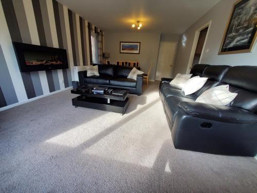 a living room with a black leather couch and a table at Aviemore Bungalow, Dalfaber in Aviemore