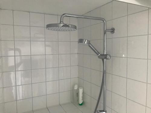 W wyłożonej białymi kafelkami łazience znajduje się prysznic z głowicą prysznicową. w obiekcie Stone street w mieście Faversham