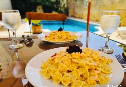 une assiette de pâtes sur une table avec deux verres à vin dans l'établissement Sannat Hills Farmhouse, à Sannat