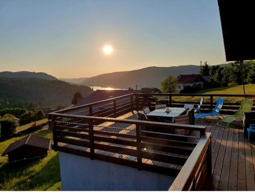 um deque com mesa e cadeiras e o pôr-do-sol em Le haut du parc em Gérardmer