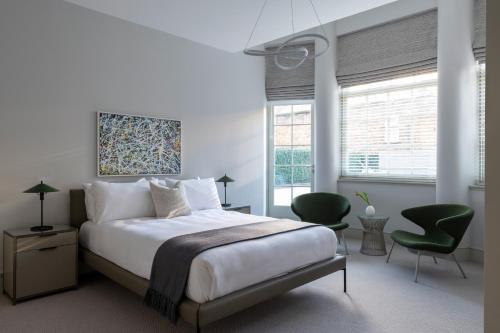 a white bedroom with a bed and two green chairs at AKA Marylebone in London