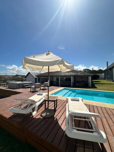 una terraza con sombrilla, sillas y piscina en Kanaloah Lodge & Cabins, en Punta del Diablo